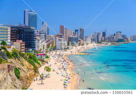 Aerial panoramic view of Calpe town, sandy beach with people, high buildings, Bahia de Calpe bay Mediterranean Sea with azure turquoise water in sunny summer day, Alicante province, Spain 130033561