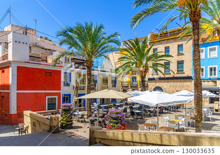 Multicolored typical buildings old houses, palm trees and street restaurant on Plaza del Quijano square in old town Alicante city historical centre in sunny summer day, Valencian Community, Spain 130033635