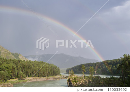 Rainbow over serene river and forest landscape with misty mountains 130033692