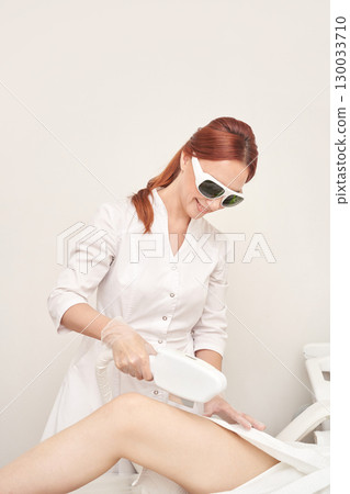 Caucasian female performing laser hair removal procedure in clinic setting 130033710