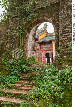 Overgrown stone steps and ancient arch framing traditional red temple gate in Hue Imperial City Vietnam 130034154
