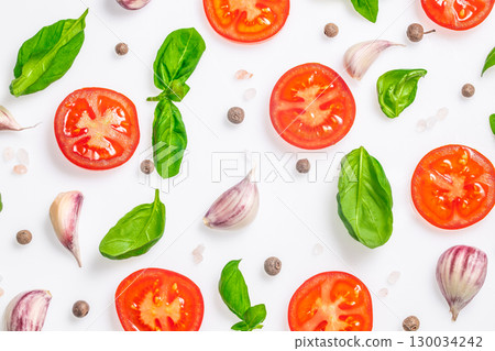Fresh tomato slices with basil leaves, garlic cloves, and peppercorns on white background. top view 130034242