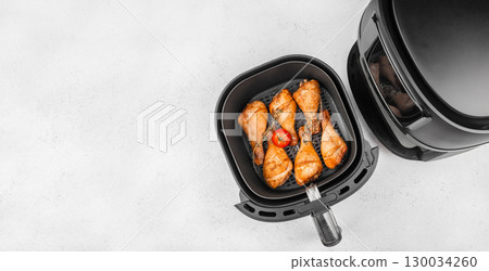 Cooked chicken drumsticks in air fryer basket with tomato and herbs. top view. copy space Cooked chicken drumsticks in air fryer basket with tomato and herbs. top view. copy space 130034260