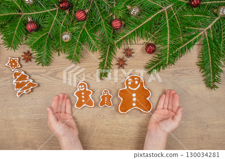Hands presenting gingerbread cookies in family concept with Christmas decorations on wooden background. top view 130034281
