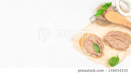 Toasted bread with creamy liver pate and fresh basil leaves on parchment. Long banner format. top view. copy space Toasted bread with creamy liver pate and fresh basil leaves on parchment. Long banner format. top view. copy space 130034335