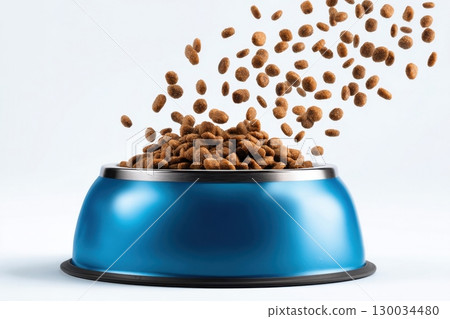 Blue steel pet bowl with small brown kibble food particles flying out of it isolated white background. Metal feline animal bowl full of dog food spilling into it. Dry cat feed floating in the air 130034480