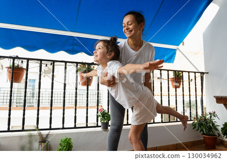 Happy Mother and Daughter Enjoying Playtime on a Sunny Home Balcony 130034962