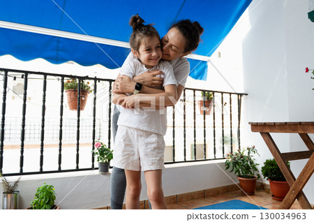 Mother Embracing Daughter on Patio Filled with Plants and Happiness 130034963