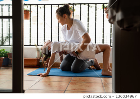 Mother Assisting Child With Yoga Practice on Balcony in Natural Light 130034967