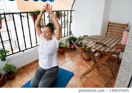 Woman Practicing Yoga on a Balcony Surrounded by Plants and Cozy Furniture 130035005