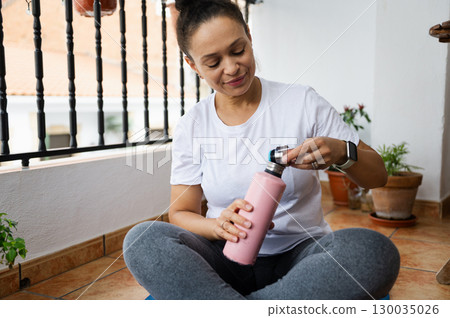 Smiling Woman Relaxing on a Balcony and Holding a Water Bottle 130035026