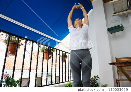 Woman Stretching on a Balcony With Blue Awning in Urban Setting 130035029