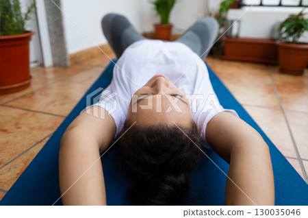 Person Practicing Relaxation Techniques on Yoga Mat at Home with Potted Plants Person Practicing Relaxation Techniques on Yoga Mat at Home with Potted Plants 130035046
