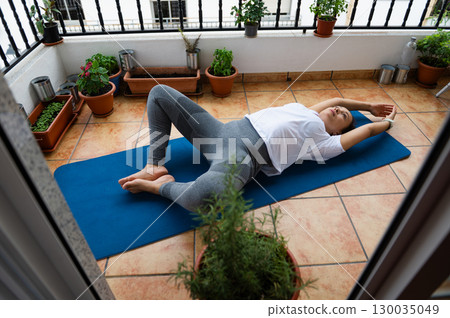 Young Woman Practicing Yoga on Outdoor Terrace with Green Plants Young Woman Practicing Yoga on Outdoor Terrace with Green Plants 130035049