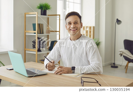 Portrait of young attractive business man working on a laptop and looking cheerful at camera. Portrait of young attractive business man working on a laptop and looking cheerful at camera. 130035194