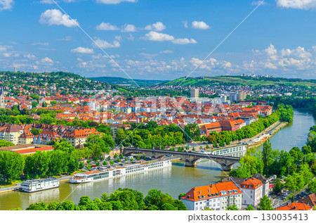 Aerial panoramic view of Wurzburg city historical center with Ludwig Bridge across Main river with touristic ships and green hills background on horizon, Lower Franconia region, Germany Aerial panoramic view of Wurzburg city historical center with Ludwig Bridge across Main river with touristic ships and green hills background on horizon, Lower Franconia region, Germany 130035413