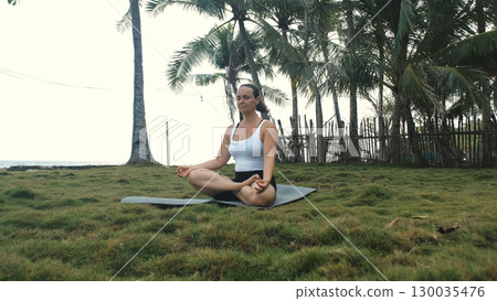 Lotus pose meditation by the ocean with woman seated on yoga mat, surrounded by calm coastal scenery  130035476