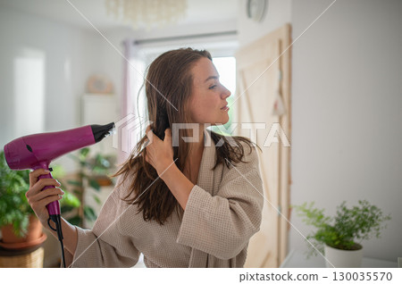 Woman blow-drying her hair after a relaxing bath. 130035570