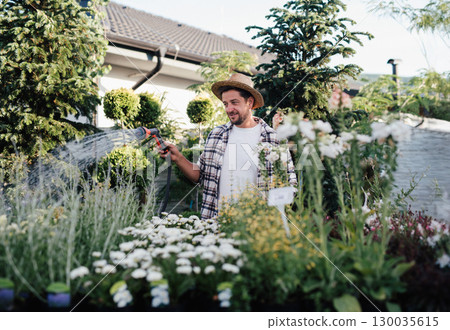 Florist caring for plants, watering them with garden hose in garden centre. Florist caring for plants, watering them with garden hose in garden centre. 130035615