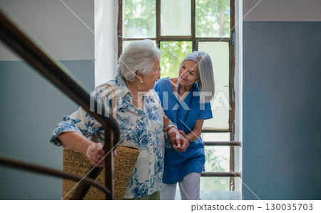 Female healthcare worker helping senior patient walking up the stairs. 130035703