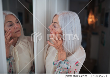 Portrait of beautiful senior woman standing in front mirror, making phone call. 130035721