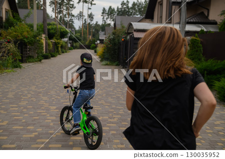 Mother and Son Playing Outdoors Boy Riding Bicycle in Suburban Neighborhood 130035952