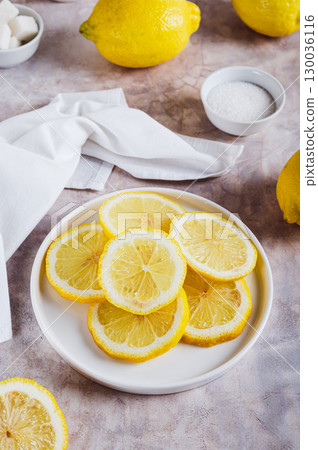 Lemons cut into juicy slices on a plate and whole on the table vertical view 130036116