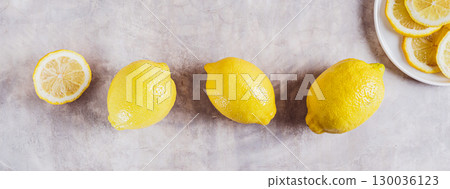 Several ripe whole lemons in a row and slices on a plate top view web banner 130036123
