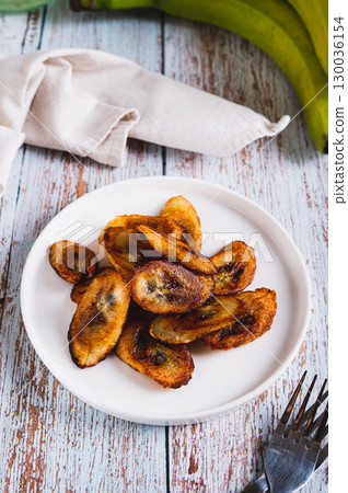 Tajadas fried banana on a plate on the table vertical view Tajadas fried banana on a plate on the table vertical view 130036154