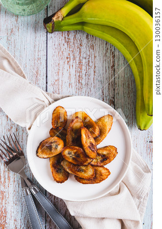 Tajadas fried banana on a plate on the table top and vertical view 130036157