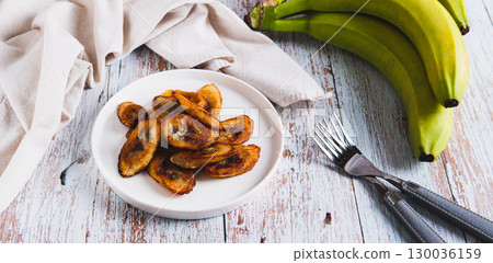 Fried plantain banana slices on a plate on the table web banner 130036159