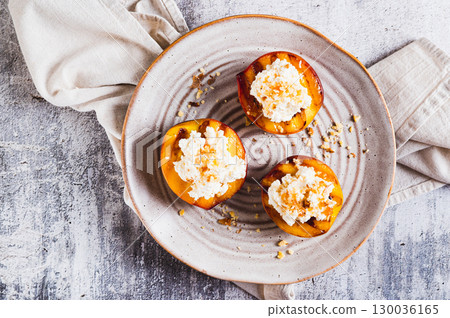 Close up of grilled peach halves with ricotta and nuts on a plate on the table top view 130036165