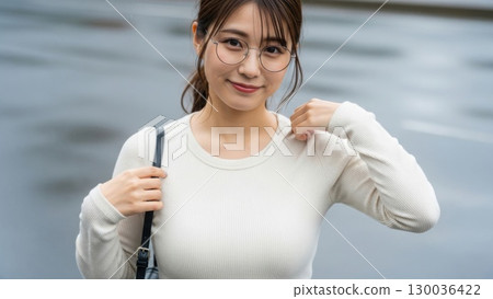 A girl with glasses smiling gently and carrying a shoulder bag in the rain 130036422