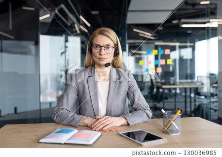 Businesswoman wearing a headset in a modern workplace with notebook and tablet on a desk. 130036985