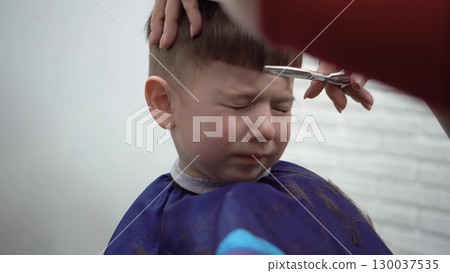 child squinting during haircut at barber child squinting during haircut at barber 130037535