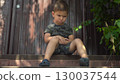 Child is angry about a bruised knee while sitting on the porch in dark clothes on a hot summer day 130037544