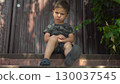Child is angry about a bruised knee while sitting on the porch in dark clothes on a hot summer day 130037545
