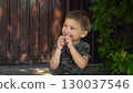 Child is sucking a lollipop sitting on the porch during a hot summer day in dark clothes 130037546