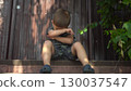 Child is angry about a bruised knee while sitting on the porch in dark clothes on a hot summer day 130037547