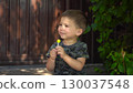 Child is sucking a lollipop sitting on the porch during a hot summer day in dark clothes 130037548