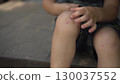 a child sits on the porch on a hot summer day he touches his scraped knee with his finger in close up wearing a t shirt and shorts 130037552