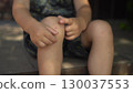 the boy sits on the porch on a hot summer day gently touching a scab on his knee with his finger the camera slowly zooms in toward his face 130037553