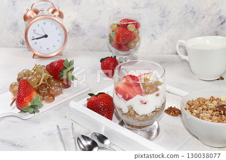 Granola with yogurt and fresh strawberries and grapes on a light table. The concept of healthy and natural food, diet useful dessert in a glass. Healthy breakfast, food for children, selective focus. Granola with yogurt and fresh strawberries and grapes on a light table. The concept of healthy and natural food, diet useful dessert in a glass. Healthy breakfast, food for children, selective focus. 130038077