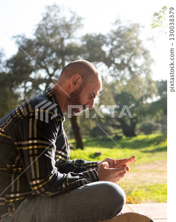 Young person using smartphone outdoors on sunny spring day 130038379