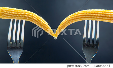 Creative culinary art featuring baby corn held by two forks 130038651