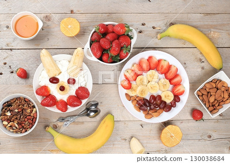 Useful breakfast of ingredients, strawberry yogurt with muesli, grapes, banana and honey on a bright table, fruit salad. Healthy and natural food concept, lifestyle, food for children, selective focus Useful breakfast of ingredients, strawberry yogurt with muesli, grapes, banana and honey on a bright table, fruit salad. Healthy and natural food concept, lifestyle, food for children, selective focus 130038684