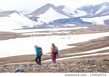 Hikers exploring the rugged terrain of Iceland's vast landscapes under a cloudy sky 130038733
