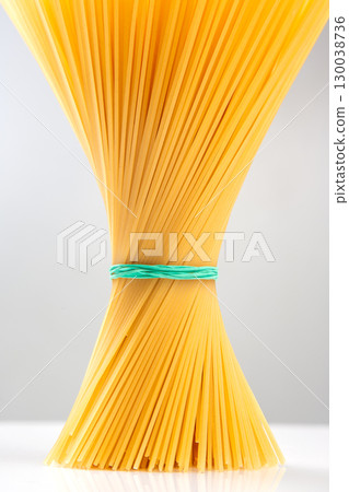Bundle of dried spaghetti noodles tied with a rubber band on a flat surface 130038736