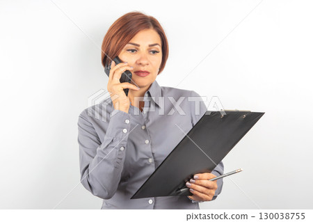 Businesswoman communicating on phone while reviewing notes in office setting 130038755