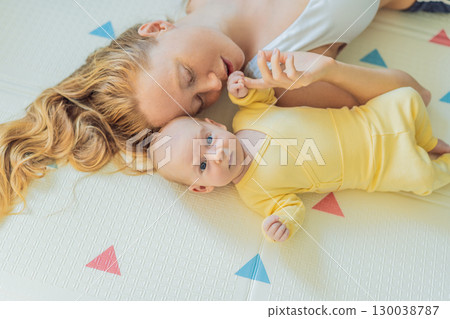 Mother and baby lying on a play mat. Tender bonding moment, cozy childhood atmosphere, and early development. Parenting, love, and infant care concept Mother and baby lying on a play mat. Tender bonding moment, cozy childhood atmosphere, and early development. Parenting, love, and infant care concept 130038787